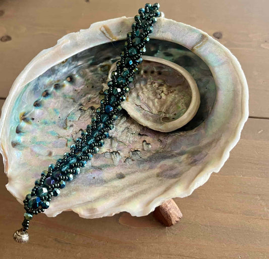 Een prachtige armband met diepe, glanzende groene tinten en elegante, gevlochten uitstraling die doet denken aan de oceaan, mystiek en natuur.