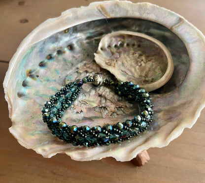 Een prachtige armband met diepe, glanzende groene tinten en elegante, gevlochten uitstraling die doet denken aan de oceaan, mystiek en natuur.