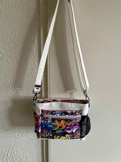  vrolijk gekleurde mini crossbody tas gemaakt van wit skai en waterafstotende stof met een kleurrijke graffiti print