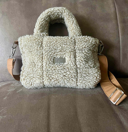 Omarm warmte en stijl met de Teddy Chic, de handgemaakte tas die comfort en elegantie perfect combineert. Gemaakt van superzachte Teddy-stof in een creamy beige tint, geeft deze tas elke outfit een knusse, luxueuze uitstraling