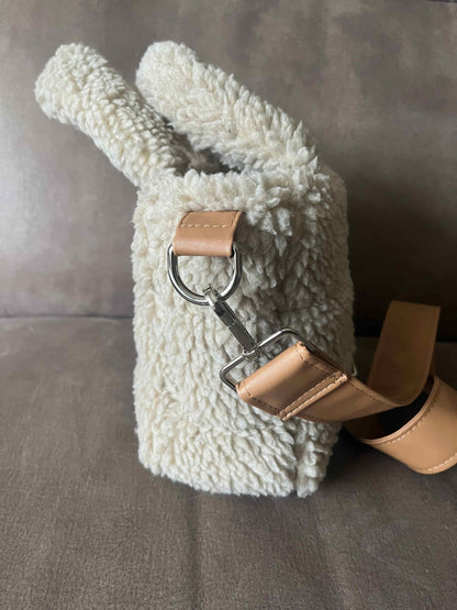 Omarm warmte en stijl met de Teddy Chic, de handgemaakte tas die comfort en elegantie perfect combineert. Gemaakt van superzachte Teddy-stof in een creamy beige tint, geeft deze tas elke outfit een knusse, luxueuze uitstraling