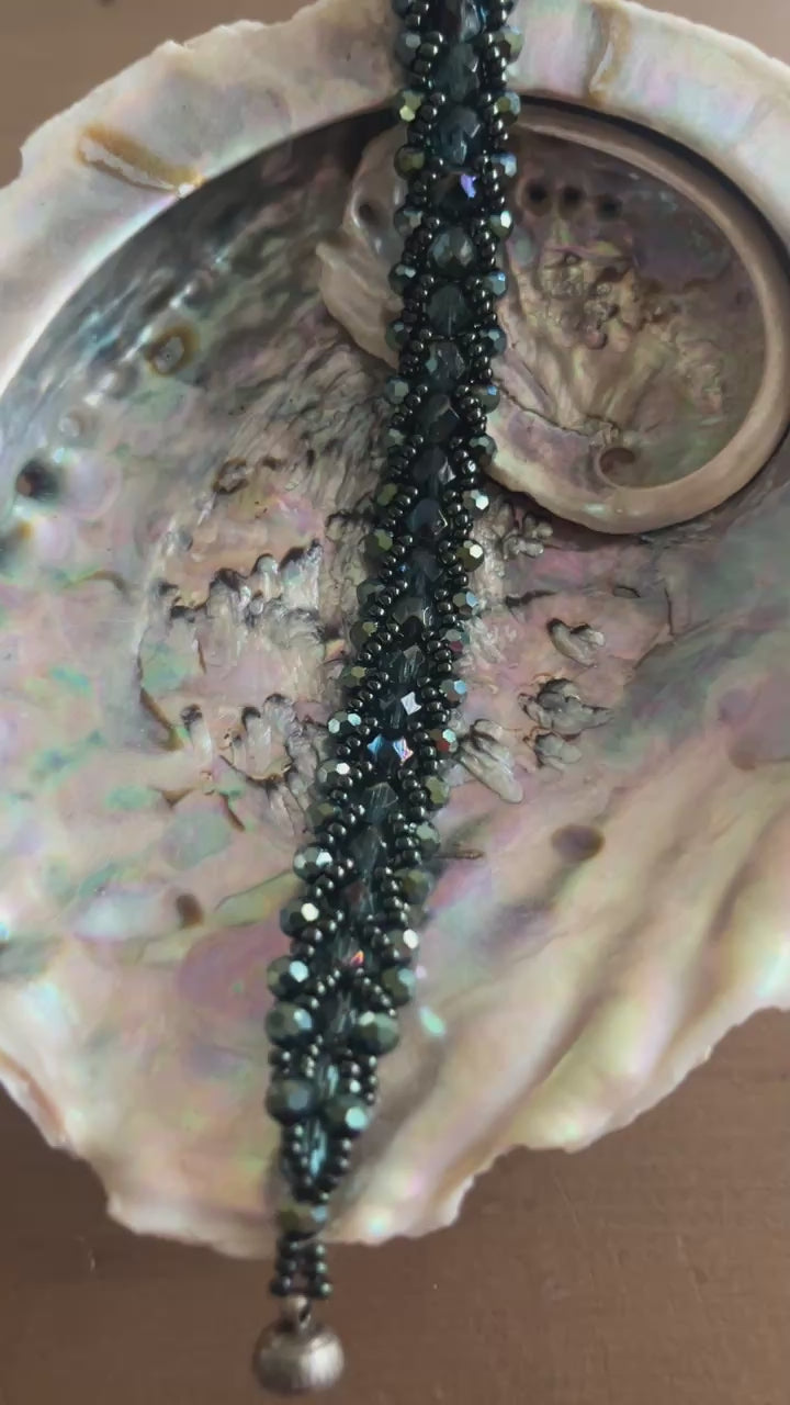 Een prachtige armband met diepe, glanzende groene tinten en elegante, gevlochten uitstraling die doet denken aan de oceaan, mystiek en natuur.